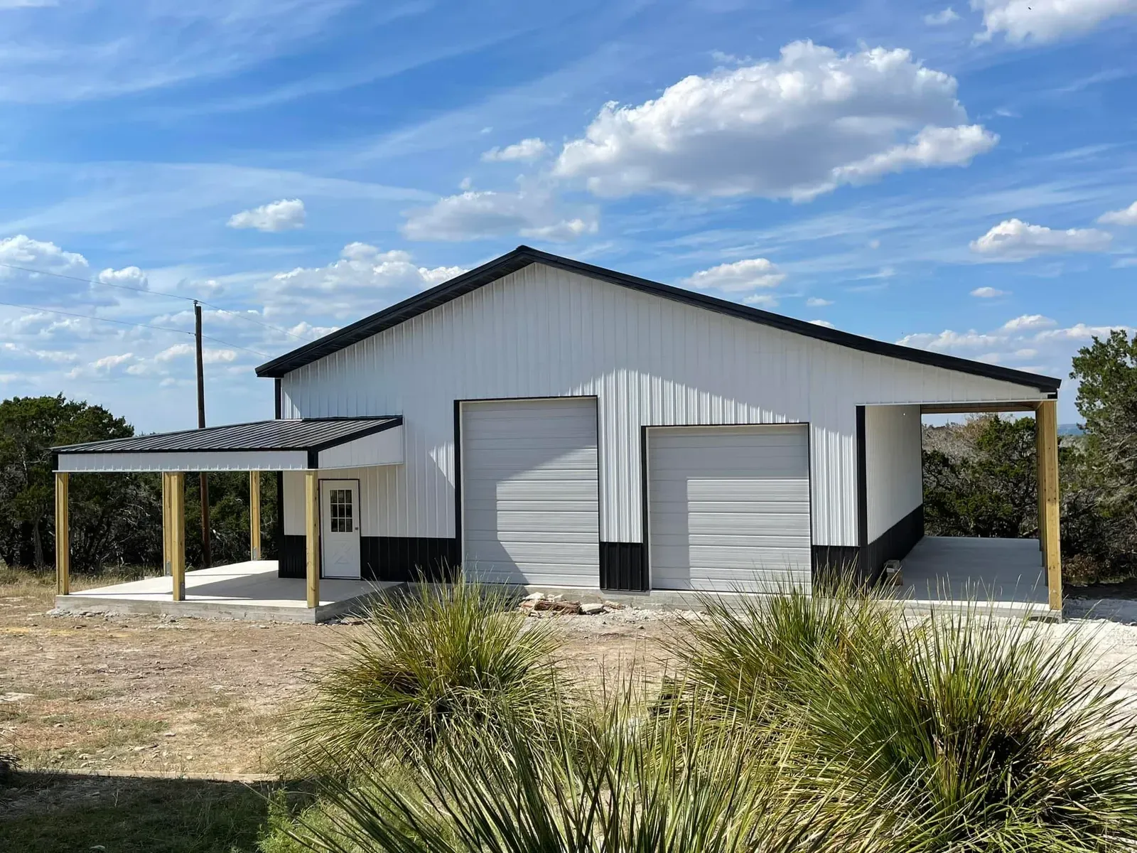 A white steel shop with black wainscot, two roll-up doors and covered porches on both ends in Texas